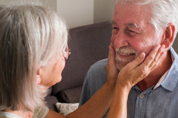 One aged woman touching face of a mature man sitting both on the sofa at home. Elderly lifestyle. Mature people enjoy life and relationship. Dating. Having care old age. Love relationship together