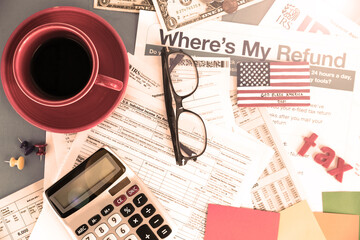 tax forms, calculator, glasses, coffee on desk. Dollars and letters TAX. View from above.