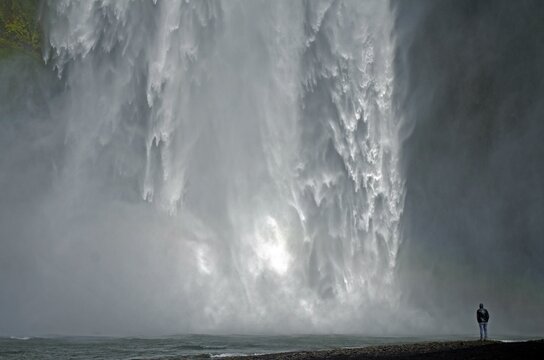Man in front of falling masses of water of a waterfall, Skogafoss, Iceland, Europe
