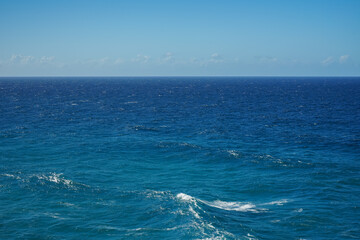 View across blue ocean to the horizon with waves in the foreground