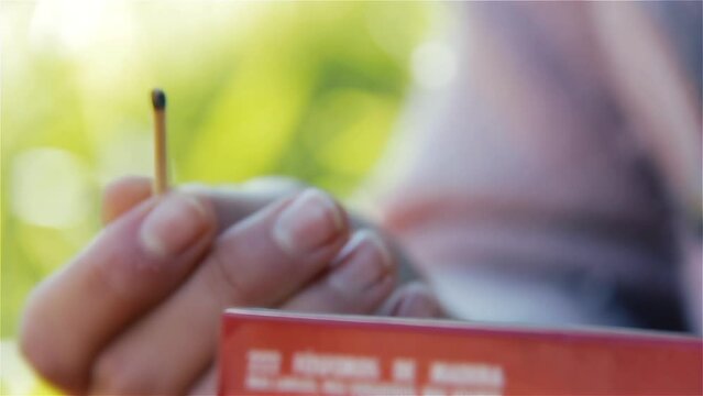 Woman Holding A Matchbox While Striking a Match Outdoors. Close Up.