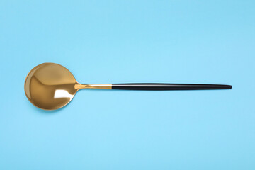 One shiny golden spoon on light blue background, top view