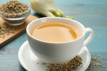 Fennel tea in cup and seeds on light blue wooden table, closeup