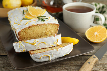 Tasty lemon cake with glaze and tea on wooden table, closeup