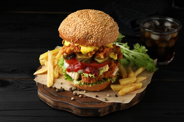Delicious burger with crispy chicken patty and french fries on black wooden table