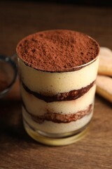 Delicious tiramisu in glass on wooden table, closeup
