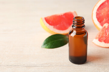 Grapefruit essential oil in bottle and fruit on light wooden table, closeup. Space for text