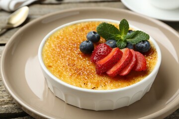 Delicious creme brulee with berries and mint in bowl on wooden table, closeup