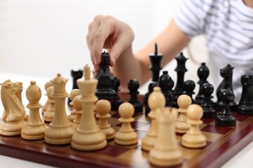 Little child playing chess at table indoors, closeup