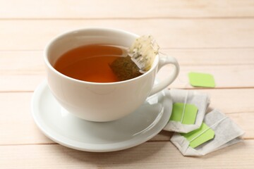Tea bags and cup of hot beverage on light wooden table, closeup
