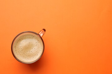 Fresh coffee in cup on orange background, top view. Space for text
