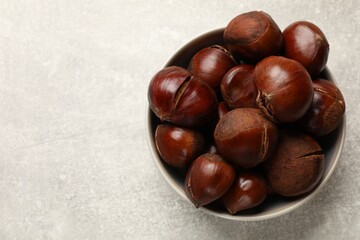 Fresh edible sweet chestnuts in bowl on grey table, top view. Space for text