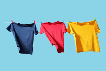 Colorful t-shirts drying on washing line against light blue background