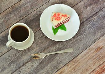 Slice of fresh mint red velvet cake, fork and cup of hot black coffee on a wooden table.