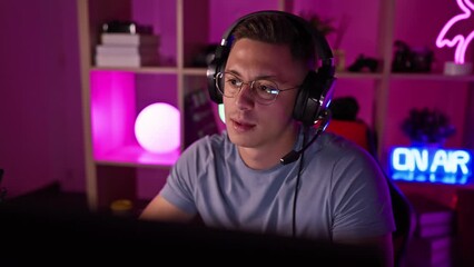 Focused hispanic man with headphones gaming in a colorful dark room at night, looking at the screen.