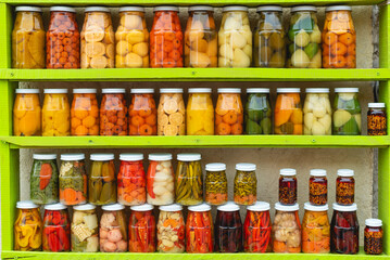 Many Jars with fruity compotes jams and pickled vegetables. Preserved fruits