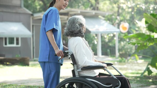 Compassionate Asian woman provides care to  elderly person in wheelchair outdoors. Engaging in physical therapy, happiness, encouraging positive environment for mature individuals with grey hair.