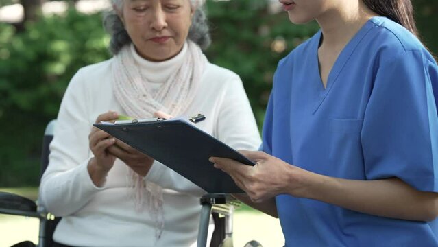 Compassionate Asian woman provides care to  elderly person in wheelchair outdoors. Engaging in physical therapy, happiness, encouraging positive environment for mature individuals with grey hair.