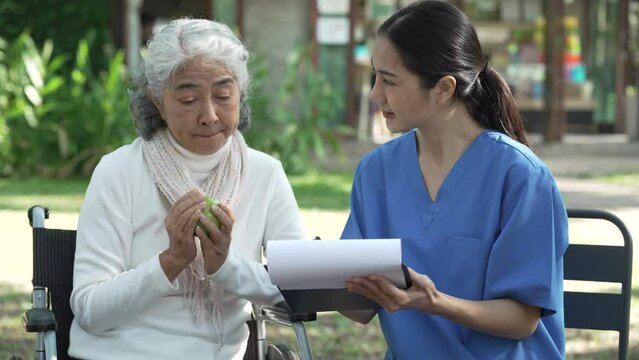 Compassionate Asian woman provides care to  elderly person in wheelchair outdoors. Engaging in physical therapy, happiness, encouraging positive environment for mature individuals with grey hair.