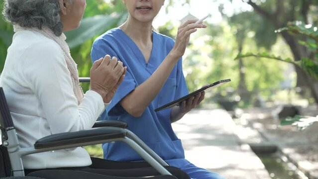 Compassionate Asian woman provides care to  elderly person in wheelchair outdoors. Engaging in physical therapy, happiness, encouraging positive environment for mature individuals with grey hair.