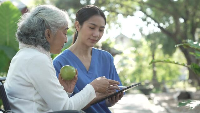Compassionate Asian woman provides care to  elderly person in wheelchair outdoors. Engaging in physical therapy, happiness, encouraging positive environment for mature individuals with grey hair.