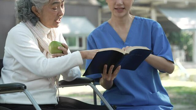 Compassionate Asian woman provides care to  elderly person in wheelchair outdoors. Engaging in physical therapy, happiness, encouraging positive environment for mature individuals with grey hair.