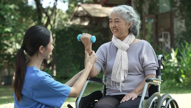 Compassionate Asian woman provides care to  elderly person in wheelchair outdoors. Engaging in physical therapy, happiness, encouraging positive environment for mature individuals with grey hair.