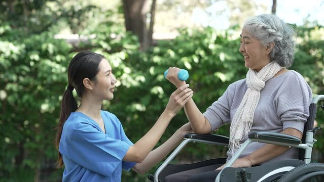 Compassionate Asian woman provides care to  elderly person in wheelchair outdoors. Engaging in physical therapy, happiness, encouraging positive environment for mature individuals with grey hair.