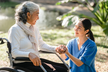 Compassionate Asian woman provides care to  elderly person in wheelchair outdoors. Engaging in physical therapy, happiness, encouraging positive environment for mature individuals with grey hair.