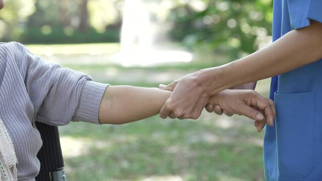 Squeeze and massage, Compassionate Asian woman provides care to  elderly person in wheelchair outdoors. Engaging in physical therapy, happiness, mature individuals with grey hair.