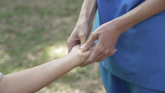 Squeeze and massage, Compassionate Asian woman provides care to  elderly person in wheelchair outdoors. Engaging in physical therapy, happiness, mature individuals with grey hair.