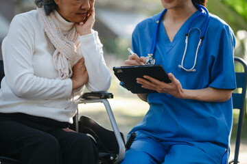 Obraz premium Compassionate Asian woman provides care to elderly person in wheelchair outdoors. Engaging in physical therapy, happiness, encouraging positive environment for mature individuals with grey hair.