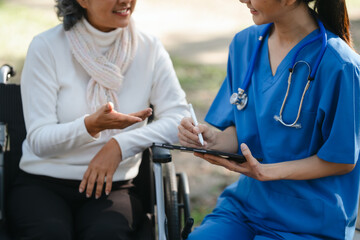 Compassionate Asian woman provides care to  elderly person in wheelchair outdoors. Engaging in physical therapy, happiness, encouraging positive environment for mature individuals with grey hair.