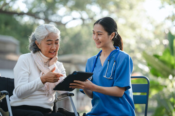 Compassionate Asian woman provides care to  elderly person in wheelchair outdoors. Engaging in physical therapy, happiness, encouraging positive environment for mature individuals with grey hair.