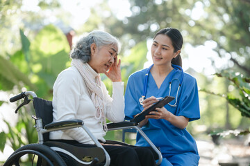 Fototapeta premium Compassionate Asian woman provides care to elderly person in wheelchair outdoors. Engaging in physical therapy, happiness, encouraging positive environment for mature individuals with grey hair.