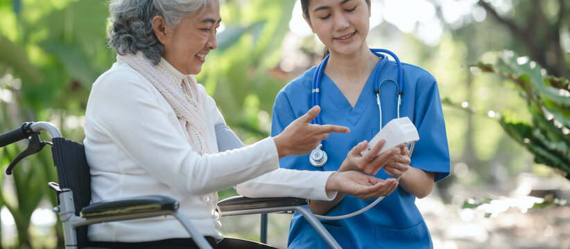 Compassionate Asian woman provides care to  elderly person in wheelchair outdoors. Engaging in physical therapy, happiness, encouraging positive environment for mature individuals with grey hair.