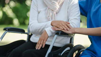 Compassionate Asian woman provides care to  elderly person in wheelchair outdoors. Engaging in physical therapy, happiness, encouraging positive environment for mature individuals with grey hair.