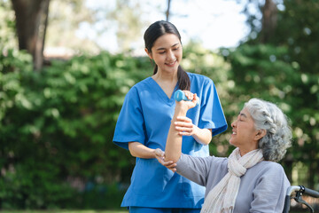 Compassionate Asian woman provides care to  elderly person in wheelchair outdoors. Engaging in...