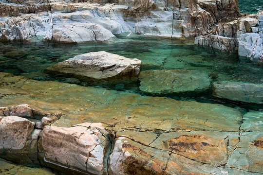 Bright aqua colored water flowing over colorful rocks and boulders at a local waterfall.