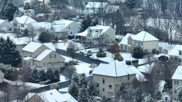 Snow-dusted suburban homes with bare trees and a quiet street. Aerial parallax of American neighborhood during snowy winter day.