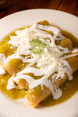 Green enchiladas. Typical Mexican dish made with a folded or rolled corn tortilla filled with shredded chicken and covered with spicy green sauce, cream, grated cheese and onion.