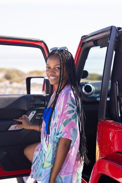 Young African American woman stands by a red car on a road trip