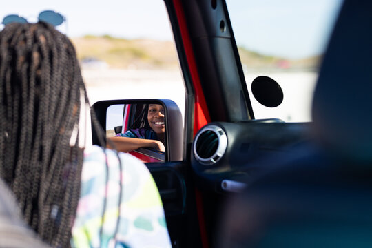 Young African American woman smiles in car side mirror on a road trip