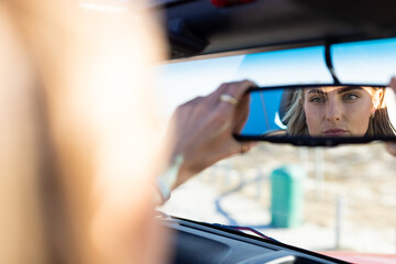 Young Caucasian woman adjusts the rearview mirror in a car on a road trip