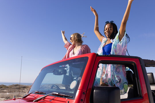 Young African American woman and young Caucasian woman enjoy a sunny day in a red convertible on a r