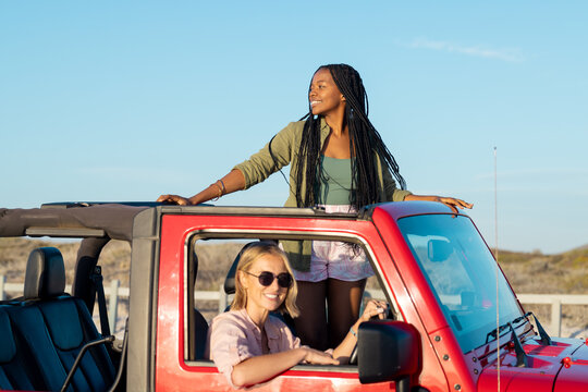 Young African American woman and young Caucasian woman enjoy a sunny day in a red jeep on a road tri