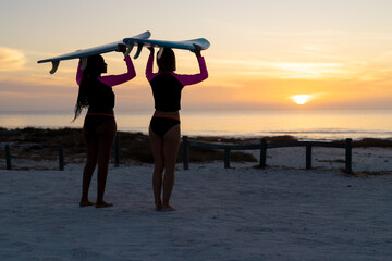 Silhouetted figures carry surfboards at sunset, with copy space