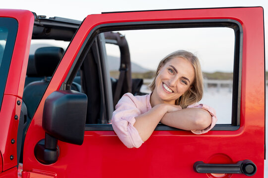 Young Caucasian woman smiles from a red vehicle on a road trip