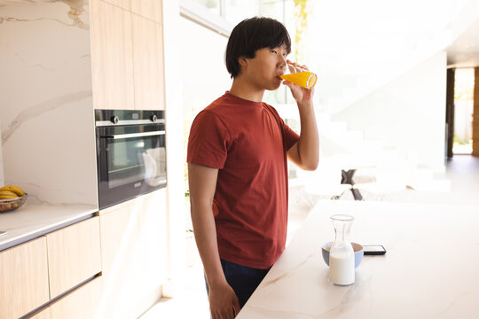 Teenage Asian boy enjoys a glass of juice in a modern kitchen