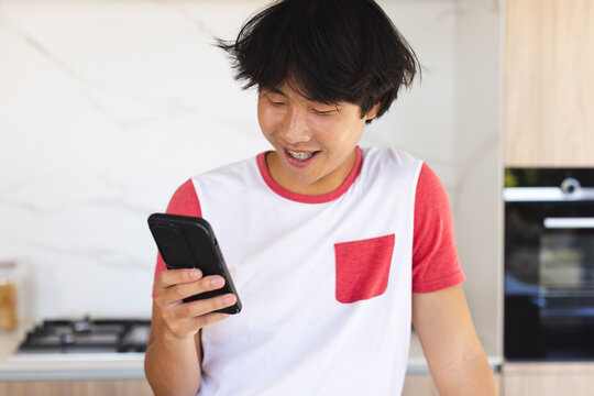 Teenage Asian boy smiles at his phone at home